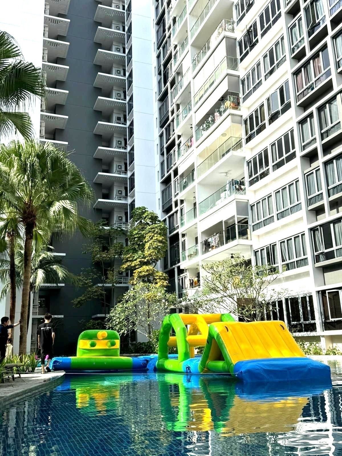 Green and yellow inflatable water obstacle course in a condominium pool between high-rise towers Singapore