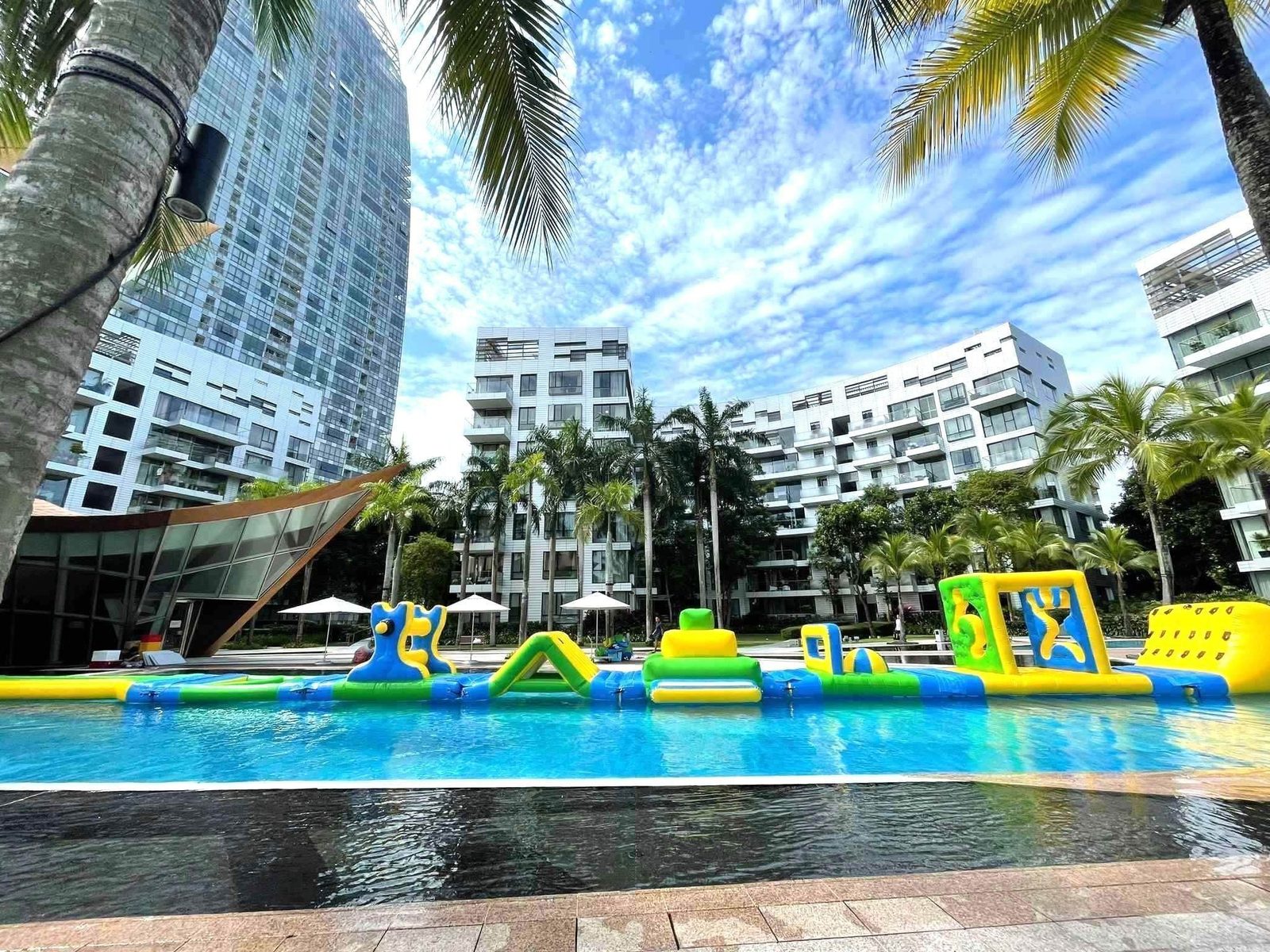 Full-length inflatable water obstacle course across a condominium pool lined with palm trees Singapore