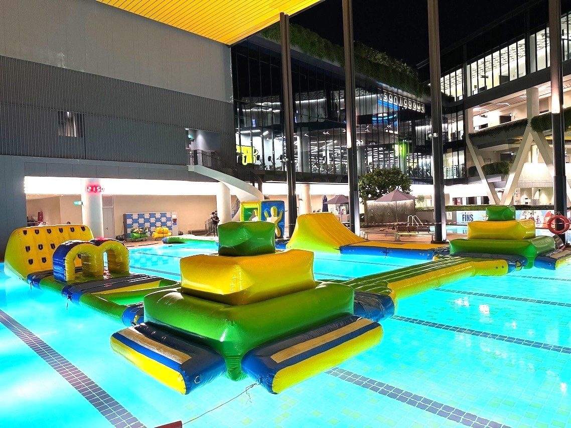 Green and yellow inflatable water obstacle platforms at an evening indoor pool event Singapore