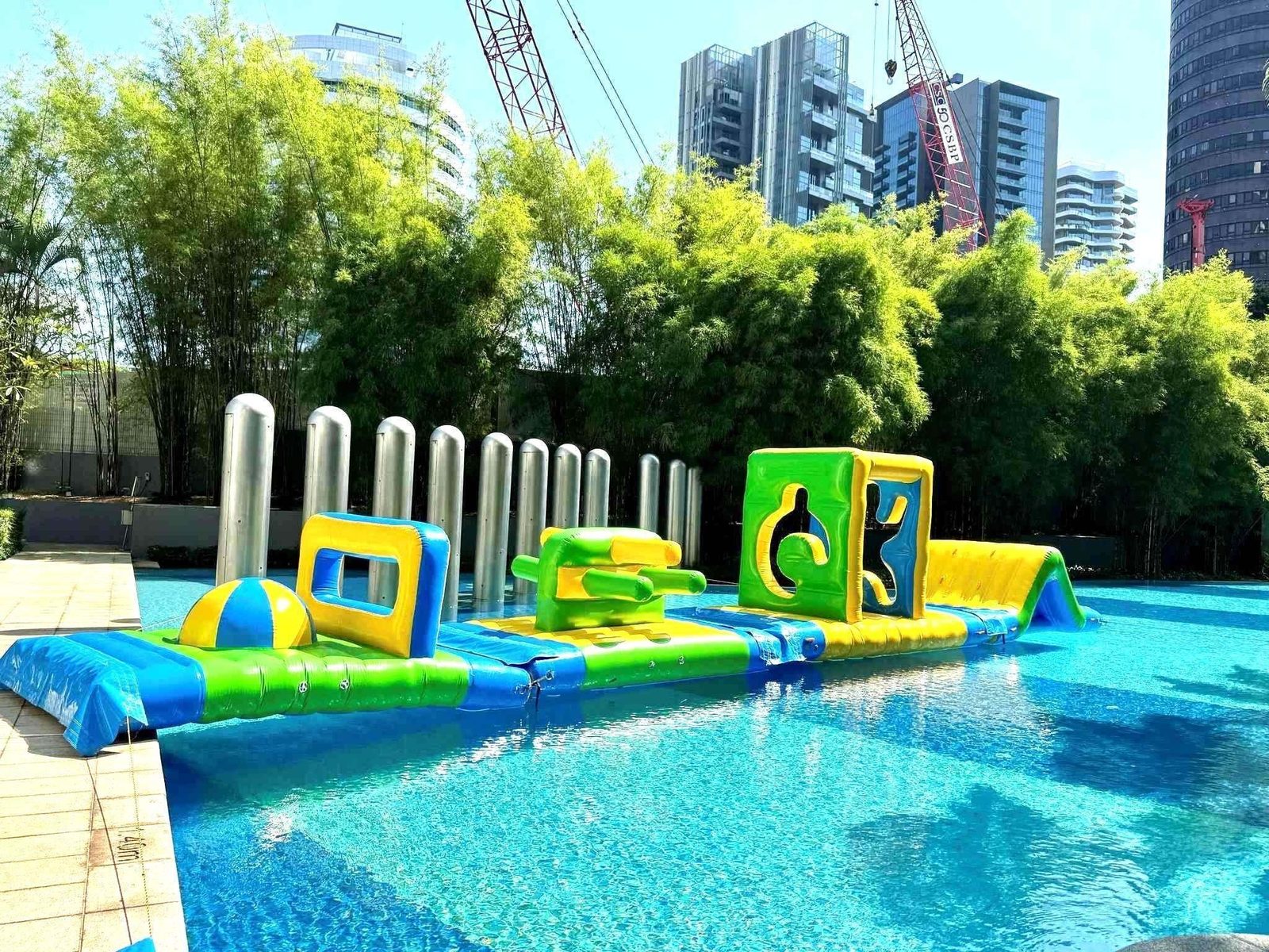 Long inflatable water obstacle course at an outdoor pool framed by bamboo Singapore