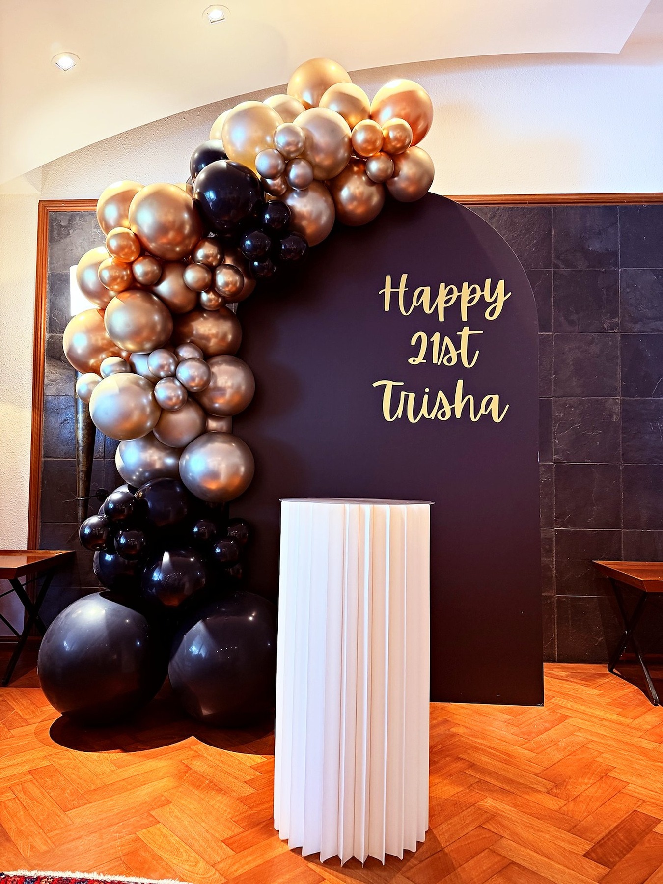 Black and rose gold birthday backdrop with a cake pedestal