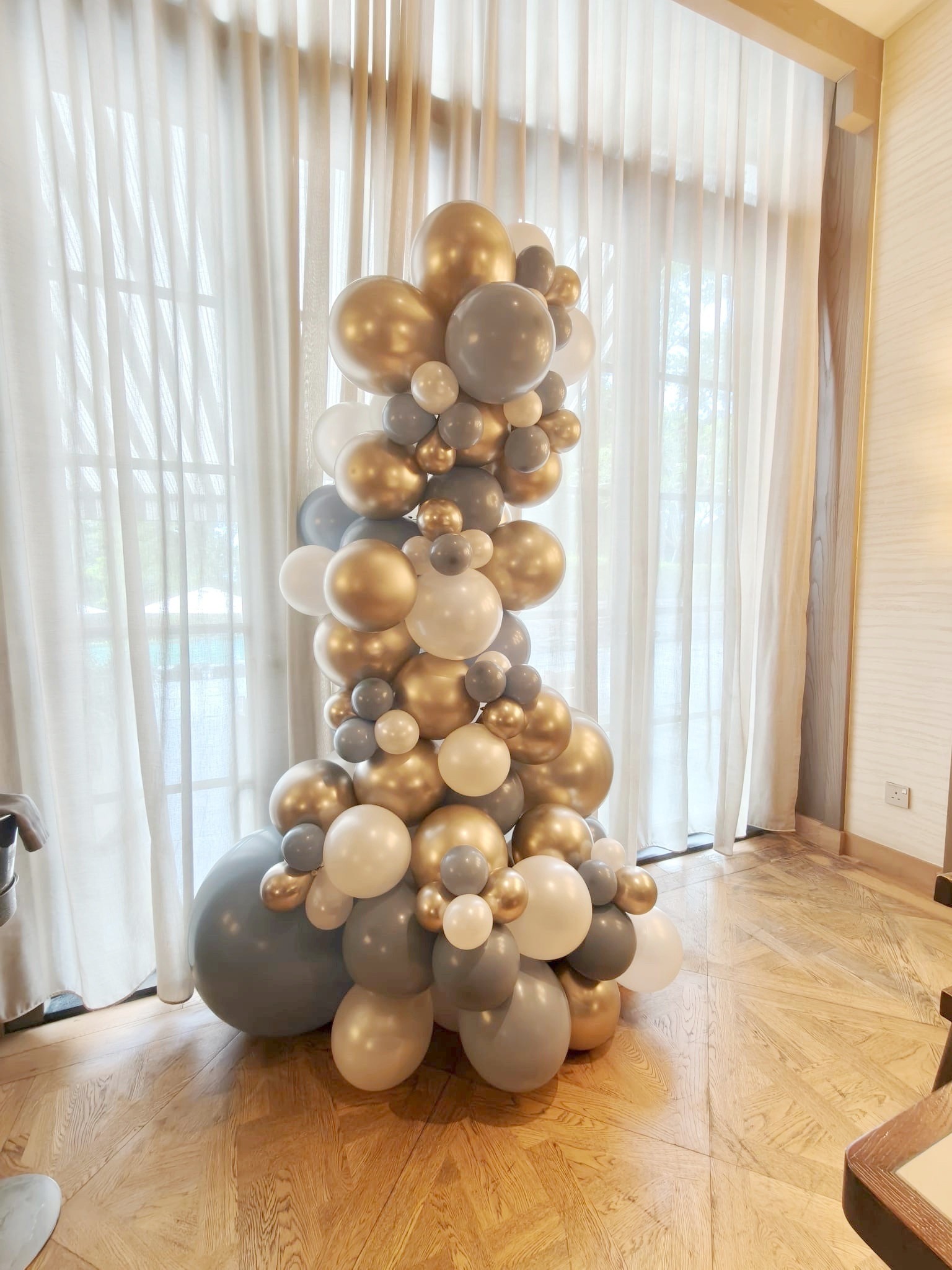 Gold grey and white organic balloon column beside curtains
